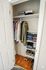 Organized closet with neatly hung clothes, stacked folded items, and shoes on a wooden floor, showcasing ample storage space.
