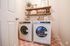 Chic laundry room featuring modern washer and dryer set with stylish wooden shelves adorned with plants and storage jars.