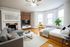 Bright and inviting living space with a modern gray sofa, cozy bed, stylish fireplace, and large windows offering ample natural light.