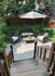 Charming outdoor patio with cozy wicker seating set under a stylish umbrella, surrounded by lush greenery for a serene retreat.