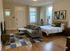 Elegant studio apartment with a cozy bed, stylish sectional sofa, and charming décor, featuring hardwood floors and an ambient floor lamp.