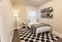 Cozy bedroom with a stylish single bed, complemented by a plush gray throw blanket, elegant floor lamp, and decorative shelves. Features a black and white checkered area rug and hardwood floors, creating a warm and inviting atmosphere.
