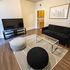 Modern living room with sleek black sofa, stylish glass coffee table, and large flat-screen TV, featuring elegant wooden flooring and contemporary decor.
