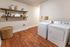 Contemporary laundry room featuring sleek washer and dryer, elegant open shelving, and warm wooden flooring for a stylish touch.