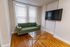 Inviting living room featuring a chic green sofa, sleek glass coffee table, and modern mounted flat-screen TV with elegant hardwood flooring.