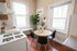 Charming kitchen with natural light streaming through large windows, featuring a cozy round dining table with modern black chairs and a stylish potted plant accenting the space.