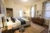 Charming bedroom with cozy decor, featuring a plush bed, stylish wooden dresser with a record player, and natural lighting from large windows.