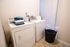 Bright utility room with modern washer and dryer, complemented by neat folded laundry and a stylish black laundry basket on tiled flooring.