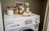 Chic laundry corner featuring a modern washer with elegant storage jars, eco-friendly dryer balls, and linen spray for a fresh touch.