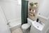 Charming bathroom with a modern touch, featuring a sleek white tub, elegant vanity, and tasteful shelving with plants and decorative items, accentuated by a soft green shower curtain.