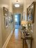 Charming hallway with elegant artwork, cozy lighting, and a rustic wooden console table, leading to a sunlit room.
