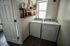 Chic laundry room with modern washer and dryer, floating shelves with stylish glass and wicker storage, and a bright window enhancing the elegant design.