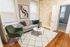 Chic living room with modern decor, featuring a cozy gray sofa, stylish green chair, and a marble coffee table on a plush patterned rug, bathed in ambient fairy light glow.