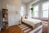 Bright, inviting bedroom featuring large windows, a cozy bed with elegant decor, and a stylish bookshelf.