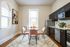 Elegant kitchen with sleek dark cabinets, a stylish dining area with pink chairs, and a chic glass table, complemented by a modern art piece on the wall.
