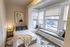 Charming bedroom with cozy bed, modern art, and inviting window seating area with natural light.