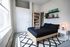 Chic bedroom with natural light, featuring a stylish black bed, sleek white nightstand, and modern shelving with shoes and decor.