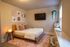 Inviting bedroom with cozy ambiance, featuring stylish artwork, a wall-mounted TV, and a modern plant hanger. Warm lighting accentuates the wooden bed and plush cushions, creating a serene retreat.