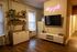 Chic living area with warm wooden flooring, modern shelving with plants and decor, and a stylish neon sign.