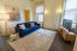 Charming living room with a plush blue sofa, elegant artwork, and abundant natural light, offering a cozy and stylish atmosphere.