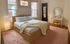 Charming bedroom with natural light, cozy modern bed, textured knit blanket, and elegant vanity corner.