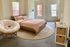 Cozy and inviting bedroom featuring a plush pink bedspread, modern wicker chair, and abundant natural light through large windows.