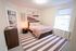 Inviting bedroom with cozy decor, featuring a soft pink knit blanket, elegant wall art, and a sunlit window creating a warm ambiance.