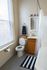 Inviting bathroom with natural light, featuring a modern vanity, stylish striped rug, and elegant shower setup.