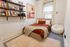 Charming bedroom with cozy earthy tones, featuring a plush bed, artistic desert-themed wall art, stylish shelves with books, and a relaxing bean bag chair by the window.