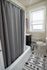 Inviting bathroom with a cozy shower, elegant gray curtain, and charming patterned rug, enhanced by natural light from a large window.