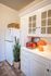 Charming kitchen corner featuring a vintage white cabinet, sleek retro red toaster, and vibrant orange lamp alongside a tall, elegant cactus.