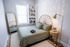 Charming bedroom with a cozy green bed, elegant rattan headboard, and ambient string lights. Features a stylish floor lamp, decorative mirror, and a bookshelf displaying books and cameras.