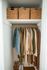 Well-organized closet with stylish clothes on wooden hangers, woven storage baskets on an upper shelf, and shoes neatly arranged below.