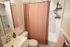 Charming bathroom with a soft pink shower curtain, sleek white vanity, stylish open shelving, and warm decor accents.