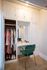 Chic closet with elegant clothing and a stylish vanity featuring makeup essentials, complemented by a plush green chair.