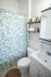 Bright and airy bathroom with elegant white fixtures, leafy green shower curtain, and rustic wooden shelves for a fresh, natural touch.