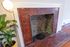 Charming red-brick fireplace with an elegant white mantle, complemented by a stylish floor lamp and lush green plant, creating a cozy and inviting living space.