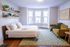 Inviting bedroom with natural light, featuring a cozy double bed, vibrant yellow sofa, and a stylish geometric rug.