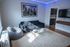 Modern living room with stylish gray couch, inviting bean bag, and sleek glass coffee table, accented by vibrant LED lighting and a cityscape artwork.