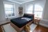Inviting bedroom with modern decor, featuring a cozy bed, natural light through large windows, and stylish shelving.