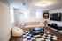 Cozy living room with a plush beige sofa, modern floor lamp, and stylish checkered rug, perfect for relaxation and entertainment.