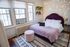 Cozy bedroom with elegant decor, featuring a plush bed with a deep purple headboard, ambient string lights, and stylish shelving. Natural light flows through large windows, creating a warm and inviting atmosphere.
