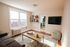 Inviting living room with a cozy sofa, natural light from large windows, modern wall-mounted TV, and stylish wooden coffee table on a plush rug.