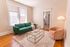 Bright living room featuring a chic green couch, stylish peach armchair, and a modern gold-framed glass coffee table on a patterned rug.