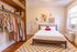Charming bedroom with elegant wooden flooring, featuring a cozy bed adorned with playful cherry cushions. The room includes a stylish open wardrobe with vibrant clothing, a modern floor lamp, and tasteful wall art.