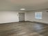 Elegant, freshly renovated room with sleek hardwood flooring, soft neutral walls, and ample natural light through a window.