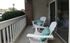 Charming apartment balcony with cozy white Adirondack chairs and vibrant teal cushions, offering a relaxing outdoor retreat.