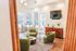 Bright and inviting clubhouse featuring modern green chairs, a stylish circular table, and sleek wood flooring. Expansive windows provide abundant natural light, while a chic media console and mounted TV complete the refined, contemporary atmosphere.