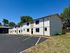 Impressive modern apartment complex with white exterior, lush greenery, and ample parking space under a clear blue sky.