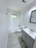 Bright, modern bathroom featuring sleek tile flooring, stylish vanity, and a classic bathtub under a sunlit window.